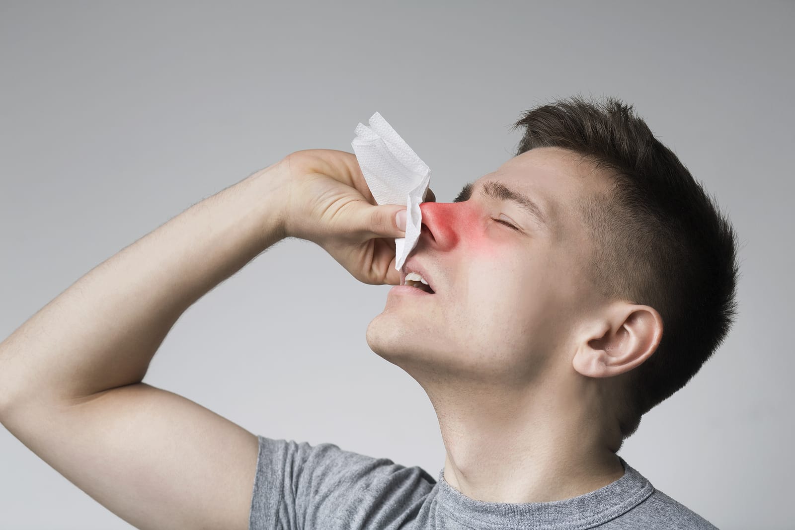 A person holding a tissue to their nose to stop a nosebleed.