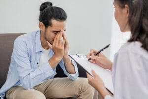 Young asian man, male has mental symptoms which must have been therapy and stress, sitting on couch to consult to psychologist during the session  taking notes to find out how to treat the therapist.