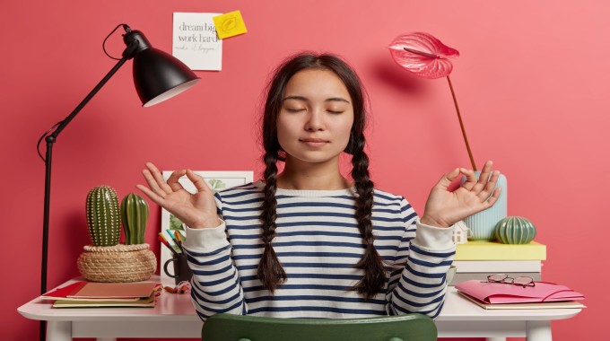 Woman sitting at a desk practicing meditation with eyes closed in a calm workspace.